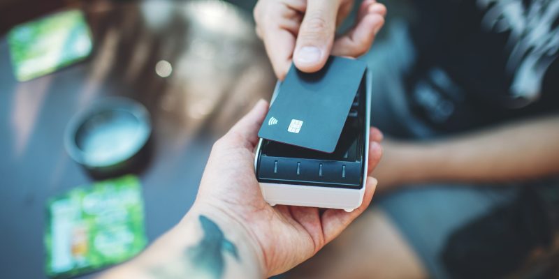 Adult man paying with credit card at cafe, close-up of hands with credit card and credit card reader